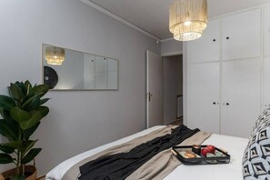 Une chambre à coucher avec un lit, une plante sur la table de chevet, un miroir et un luminaire suspendu.