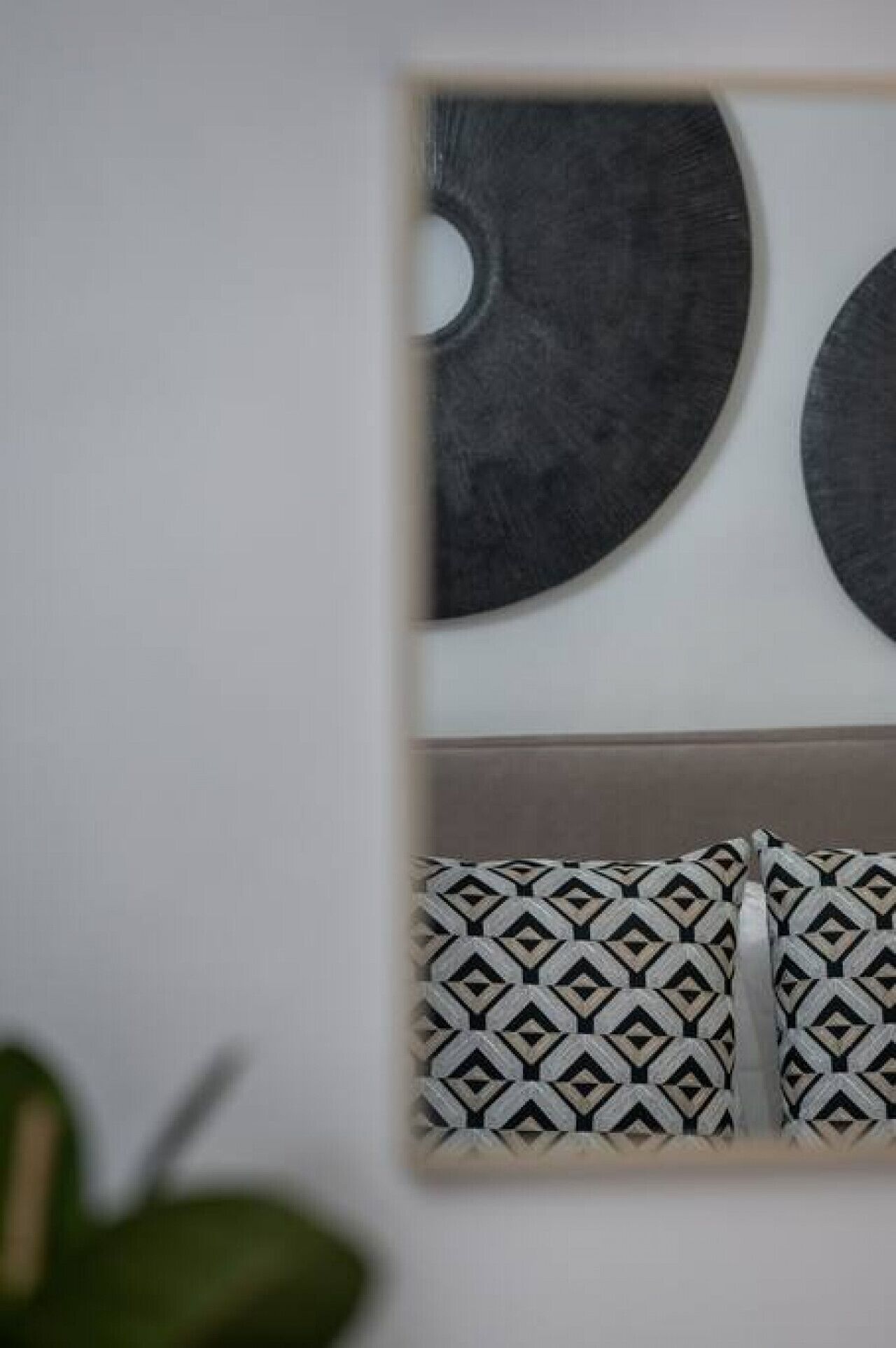 Une pièce avec un mur blanc, un objet rond de couleur sombre et des coussins à motifs.