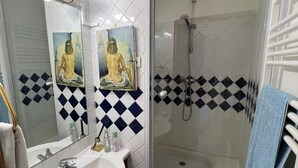 Un baño con lavamanos blanco, espejo, ducha y suelo de baldosas.