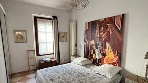 Un dormitorio con una cama grande, una ventana con cortinas, un radiador y un cuadro en la pared.