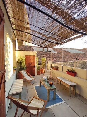 A covered patio with a view of the countryside, featuring a table with a bowl of fruit, a bottle, and glasses, surrounded by lounge chairs and potted plants. - Ancienne Savonnerie 5 minutes from Palais Longchamp - 100m2 + shaded terrace (Marseille)