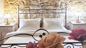 A bedroom with a stone wall, a metal bed frame, white bedding, and a hanging light fixture.
