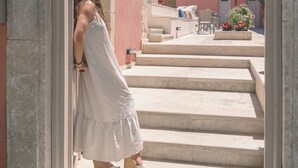 A woman in a white dress and hat entering a building with a stone staircase and a pink wall.