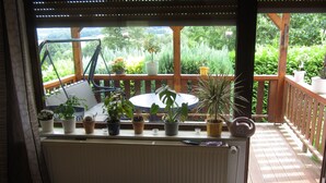 A balcony with a view of a garden, a table, and various potted plants.