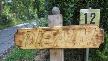 A wooden signpost with the name 'DIE ALM' carved into it, mounted on a post with a stone at the top.