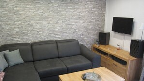 A modern living room with a grey sectional sofa, a wooden coffee table, and a stone-textured wall.