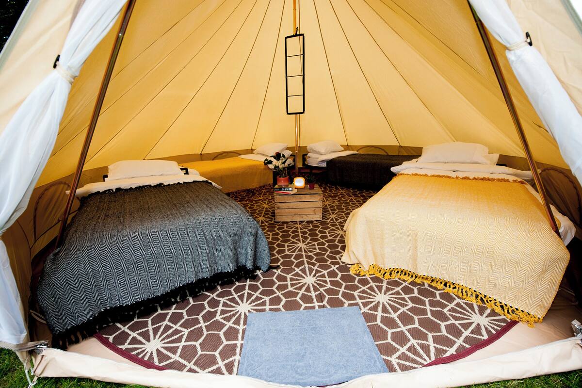 Uma tenda com duas camas, uma luminária pendente e uma pequena mesa com uma vela.