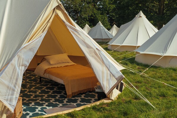 A series of dome-shaped tents with a single bed inside, set on a patterned floor, surrounded by grass and trees.