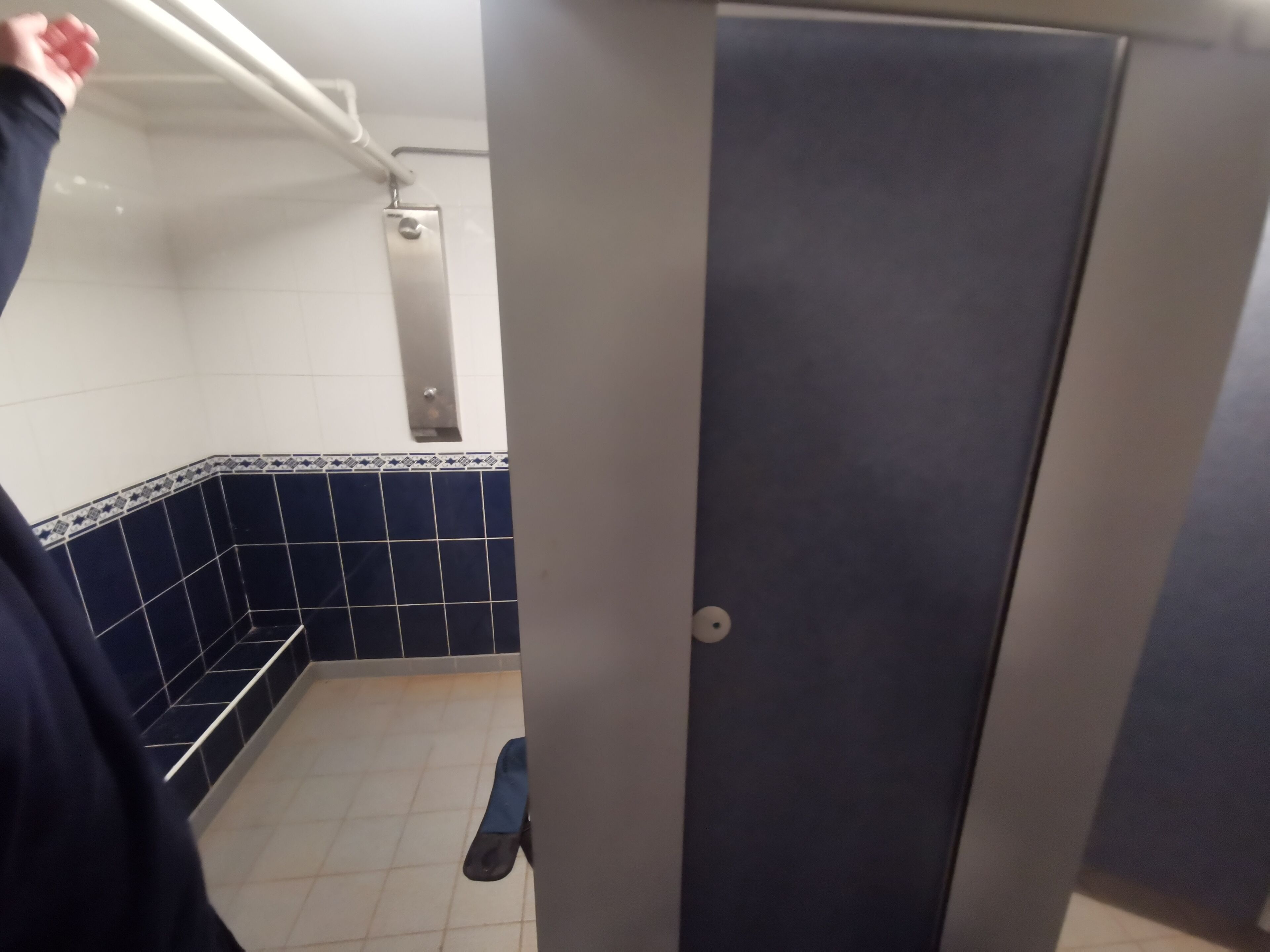 A restroom with blue and white tiled walls, a metal handrail, and a door.