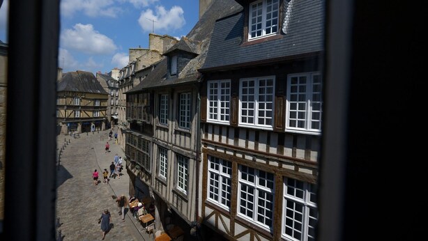 A traditional European street with half-timbered buildings, cobblestone pavement, and outdoor seating areas. - Guest House Saint Yves (Dinan)