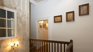 A wooden staircase with a railing, a wooden floor, and a white ceiling with exposed beams. There are framed pictures on the wall and a window with a view of the outside. - Guest House Saint Yves (Dinan)