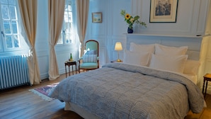 A bedroom with a large bed, a chair, a lamp, a radiator, and a window with curtains. - Guest House Saint Yves (Dinan)