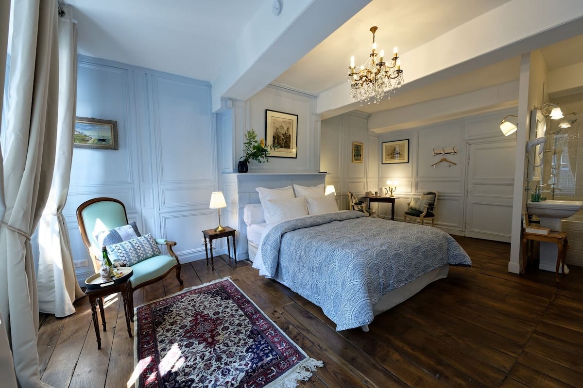 A bedroom with a large bed, a chandelier, a chair, and a nightstand.