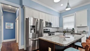 A modern kitchen with white cabinets, stainless steel appliances, and a granite countertop island with bar stools. - Fun & Renovated Artsy Downtown Apt Dog Friendly with Fully Fenced Backyard and Private Parking (Savannah)
