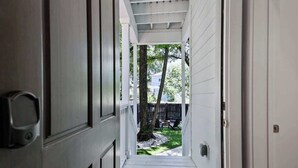 A narrow hallway with white walls and a wooden floor leading to an outdoor area with a tree and a fence. - Fun & Renovated Artsy Downtown Apt Dog Friendly with Fully Fenced Backyard and Private Parking (Savannah)