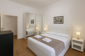 Quarto de hotel com cama, mesas de cabeceira, espelho, guarda-roupa e um quadro na parede.
