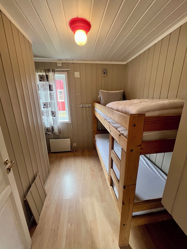 A small, cozy room with a bunk bed, wooden walls, a window with curtains, and a ceiling light. - Sanda Camping (Midt-Telemark)