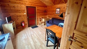 A cozy cabin interior with a wooden floor, a dining table with chairs, a sofa, a TV on a small table, and a red door. - Sanda Camping (Midt-Telemark)