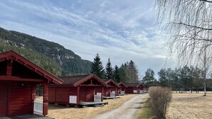 A row of red wooden cabins with a gravel path leading to them, set against a backdrop of mountains and trees. - Sanda Camping (Midt-Telemark)