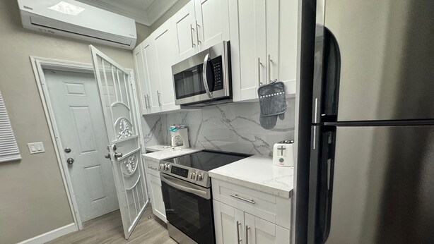 Una cocina moderna con armarios blancos, un refrigerador de acero inoxidable, un microondas, un tostador y un horno.