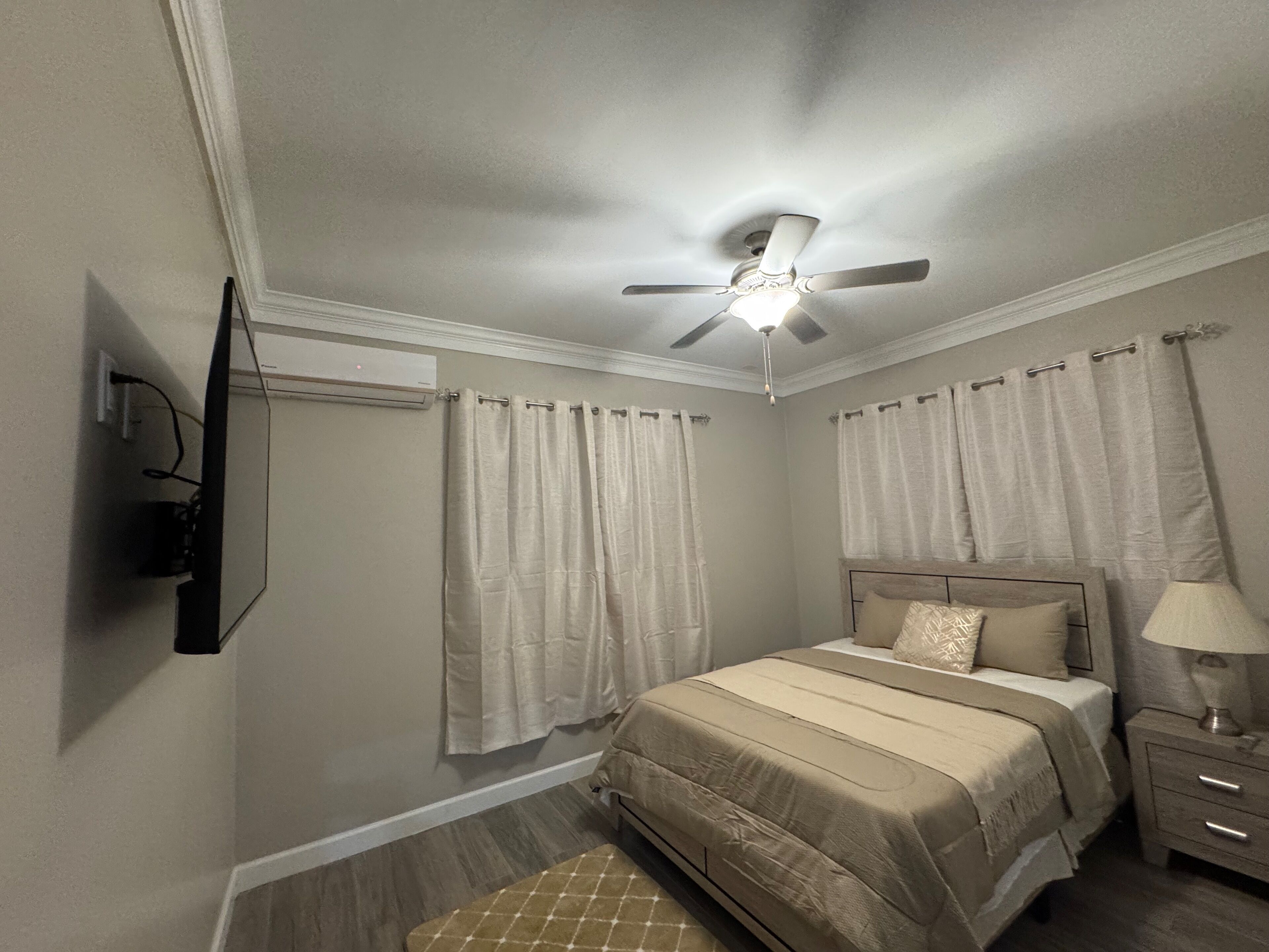 Une chambre à coucher avec un lit, un ventilateur de plafond, une table de chevet et une lampe.