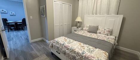 Un dormitorio con cama, mesita de noche, lámpara, armario y zona de comedor con sillas y mesa.