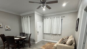 Amplia sala de estar con mesa de comedor, sillas, sofá, ventilador de techo y una puerta.