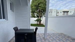 Un patio con una mesa y sillas, un muro blanco y vistas a un edificio y un árbol.