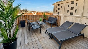 Eine Dachterrasse mit Holzboden, Metallstühlen, einem Tisch und Liegestühlen.