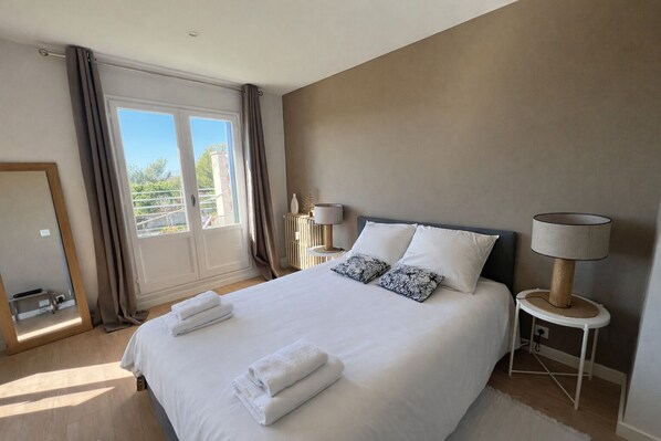 A hotel room with a large bed, two bedside lamps, a mirror, and a view of the outdoors.