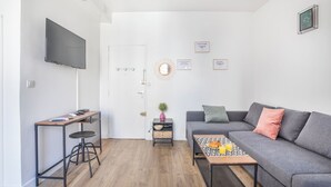 Ein modernes Wohnzimmer mit einem grauen Sofa, einem Couchtisch mit Orangensaft, einem an der Wand befestigten Fernseher und einem kleinen Beistelltisch mit einer Pflanze.