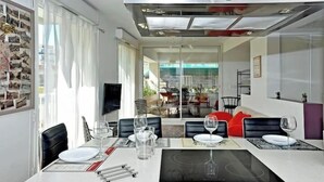 Un comedor moderno con un separador de vidrio, un televisor de pantalla plana y una mesa de comedor preparada para seis personas, con copas de vino y platos.