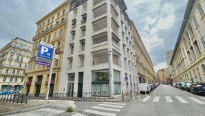 Un edificio de varios pisos con balcones, un paso de peatones y coches aparcados.