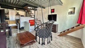 A modern interior with a wooden dining table, a hanging chair, a staircase, and a kitchen area. - Le Panier- Superb duplex with sea view, terrace and spa bath (Marseille)