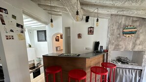A modern kitchen with a central island, red bar stools, hanging light bulbs, and a rustic ceiling. - Toit Vieil - Terrace with stunning view over Aix rooftops (Aix-en-Provence)