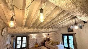 A rustic living room with exposed wooden beams, a white brick wall, a sofa, a coffee table, and a guitar. - Toit Vieil - Terrace with stunning view over Aix rooftops (Aix-en-Provence)