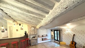 A rustic interior with exposed wooden beams, a bar area with red stools, a bookshelf, and a guitar. - Toit Vieil - Terrace with stunning view over Aix rooftops (Aix-en-Provence)