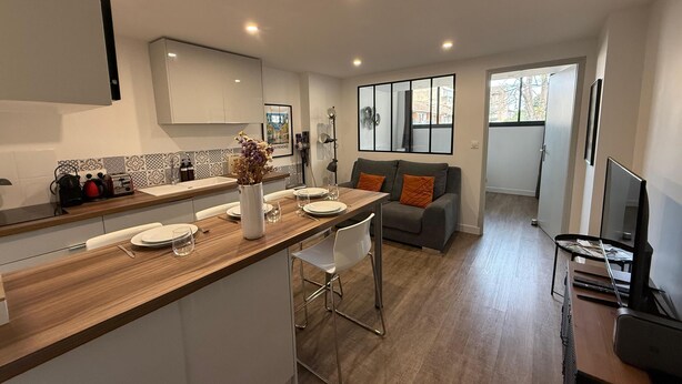 A modern kitchen with a wooden countertop, white cabinets, and a dining area with a grey sofa and orange cushions. - L'Amandier - Lovely New 2-Bedroom apt in Aix City Center (Aix-en-Provence)