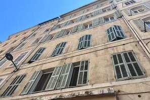 Un edificio de varios pisos con fachada color beige y múltiples ventanas con contraventanas.