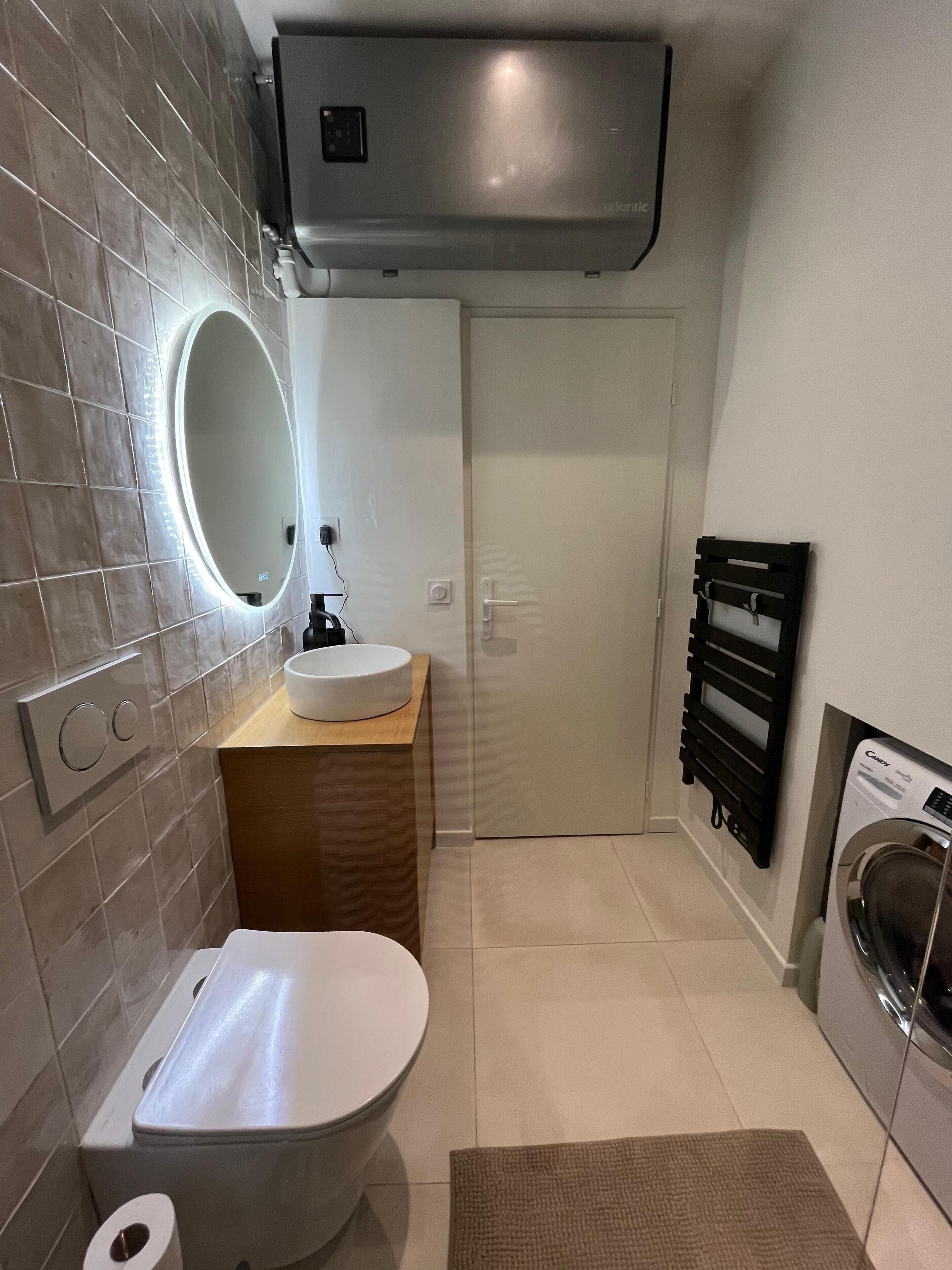 A modern bathroom with a toilet, sink, mirror, and built-in heater.
