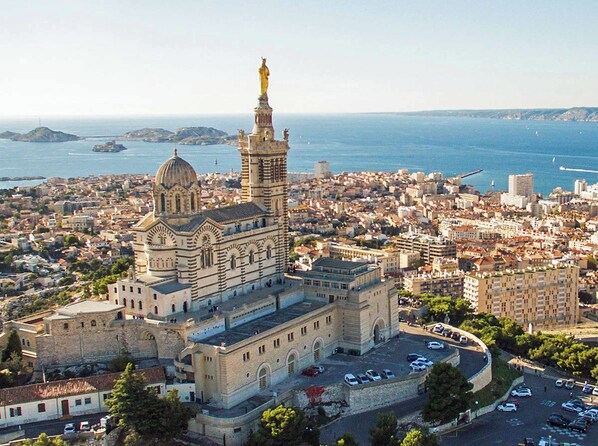 A historic building with a prominent dome and a statue on top, surrounded by a densely packed urban area with visible roads and parked cars.