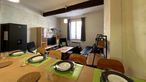 A dining area with a wooden table set for four, a television, and a bookshelf. - Chez Florence - Spacious 1BR in Historic City Center (Aix-en-Provence)