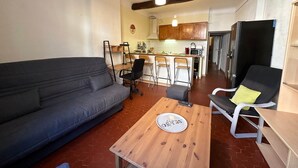 A compact living space with a sofa, a dining table, and a kitchenette in the background. - Chez Florence - Spacious 1BR in Historic City Center (Aix-en-Provence)