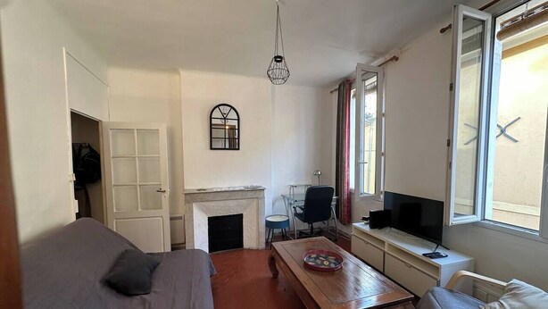 A room with a bed, a wooden table, a TV, a fireplace, and a window with curtains. - Chez Monique - 1BR in historic city center, mairie square (Aix-en-Provence)
