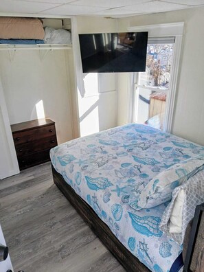 Un dormitorio con cama, televisor montado en la pared, ventana y cómoda de madera.