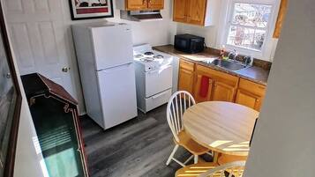 Une cuisine équipée d’une cuisinière, d’un four à micro-ondes et d’un réfrigérateur, avec des meubles de rangement en bois et un coin repas comprenant une table et des chaises.