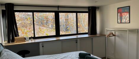 A bedroom with a bed, a window with curtains, a radiator, a coat rack, and a painting on the wall.