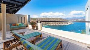 Un balcón con vistas al mar, una zona de estar con cojines y una planta en maceta.