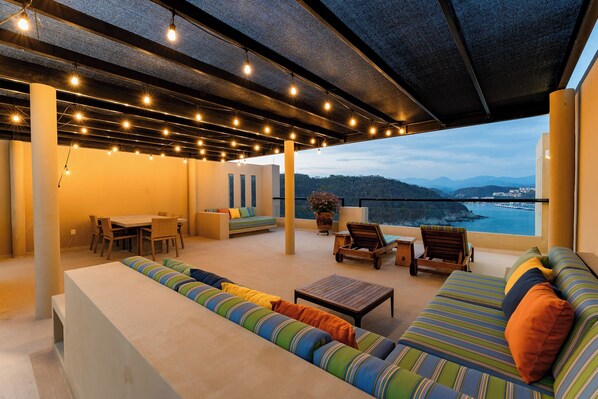 A spacious outdoor seating area with a view of the sea, featuring a sofa, chairs, and a dining table. - Coastal Views and Private Beach Access (Huatulco)