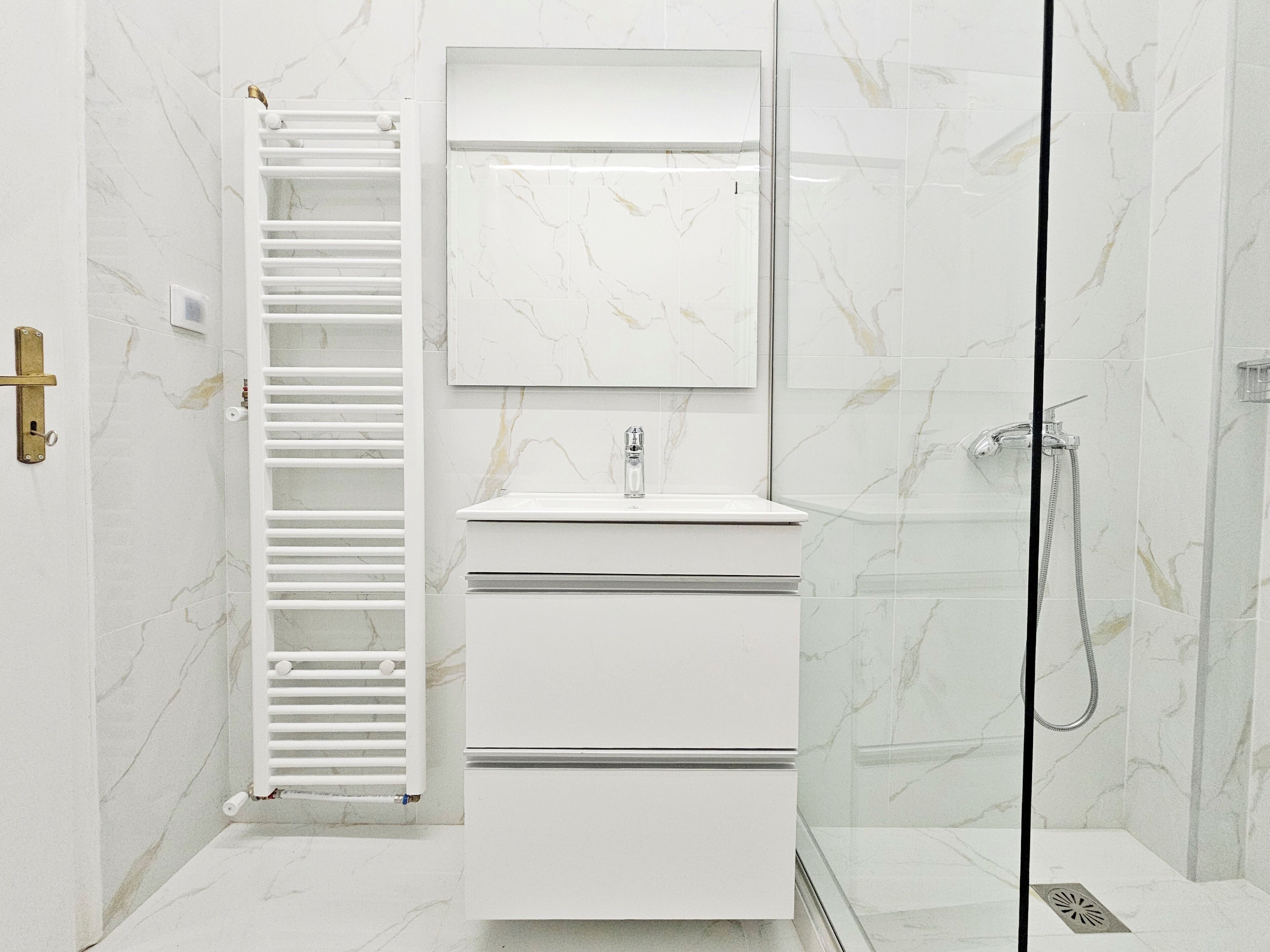 Un baño moderno con cabina de ducha de vidrio, tocador blanco con espejo y perchero.